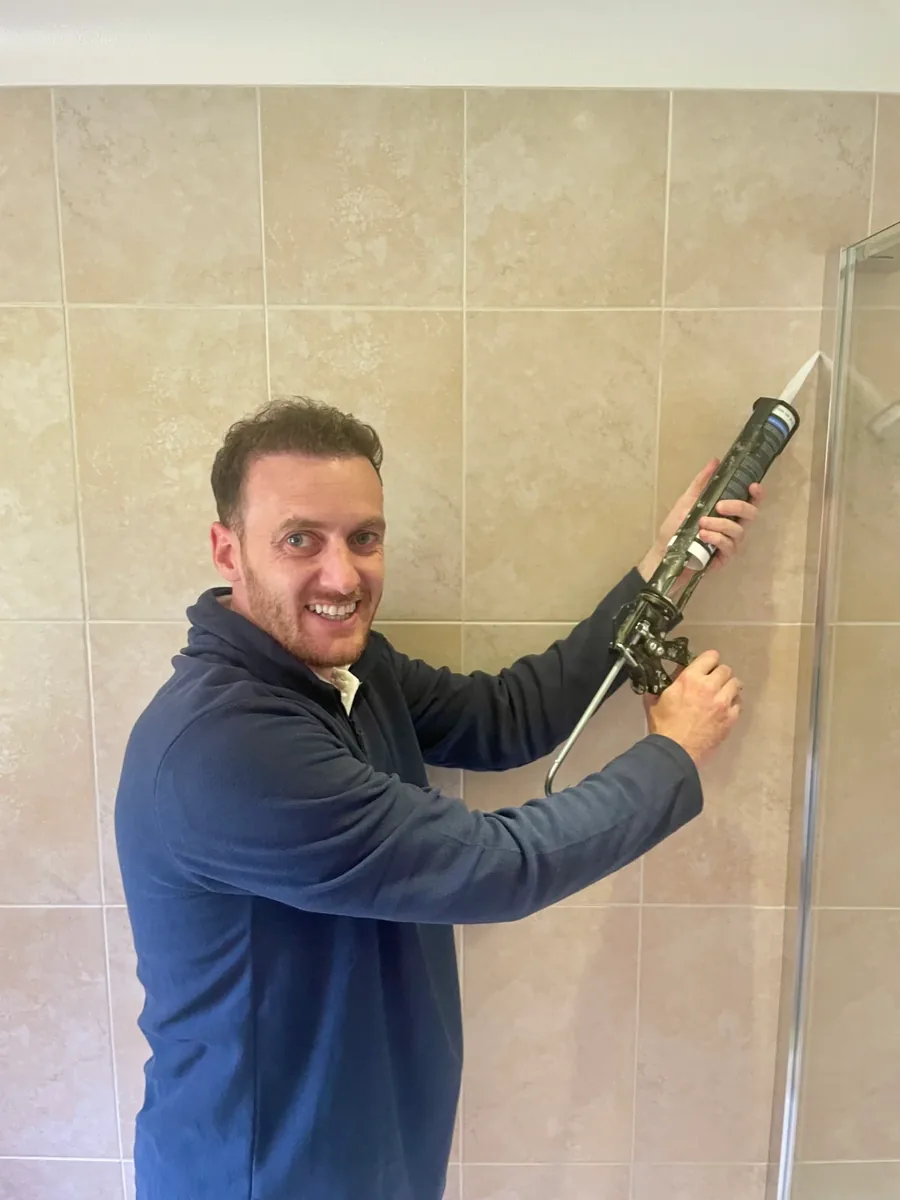 Mr Mastic applicator sealing the vertical joint between a glass shower screen and tiled wall